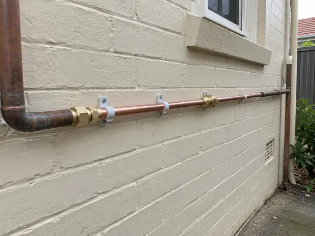 Repaired copper water pipe fixed along an exterior brick wall beneath a window in Hurstville